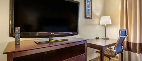 Habitación de hotel con un televisor de pantalla plana grande sobre un aparador de madera, un escritorio con una silla, una lámpara y un cuadro en la pared.