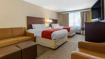 A hotel room with two beds, a sofa, a TV, and a desk.