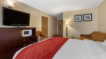 A hotel room with a bed, a TV, a microwave, a desk, a chair, and two framed pictures on the wall.