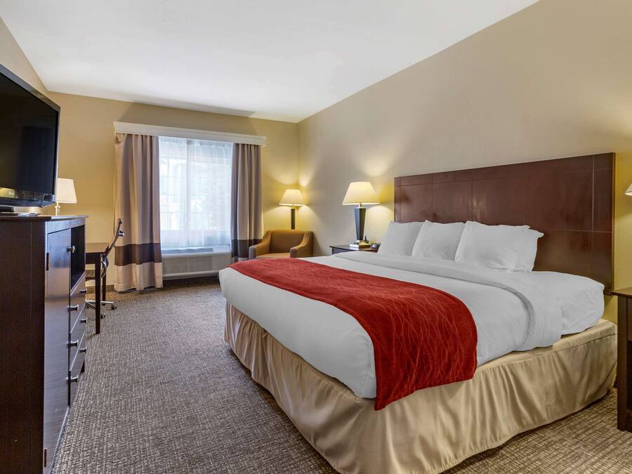 A hotel room with a large bed, two bedside lamps, a television, a desk with a lamp, and a window with curtains.