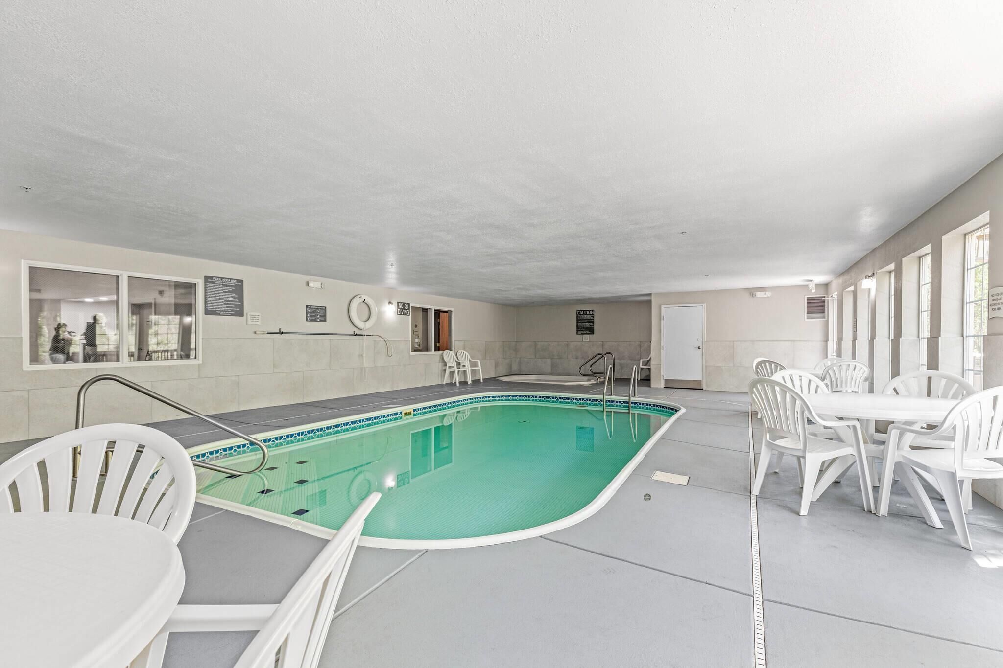 An indoor swimming pool with a tiled floor, a poolside table, and white plastic chairs.