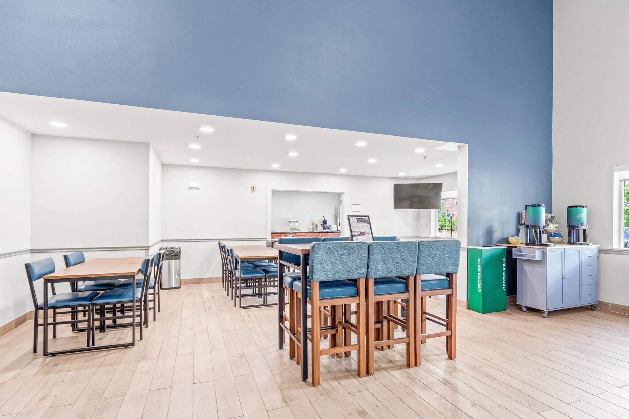A modern dining area with tables and chairs, a kitchen area, and a water dispenser.