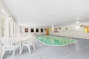 Una piscina interior con mesa y sillas, un cartel de zona de buceo y un flotador en la pared.