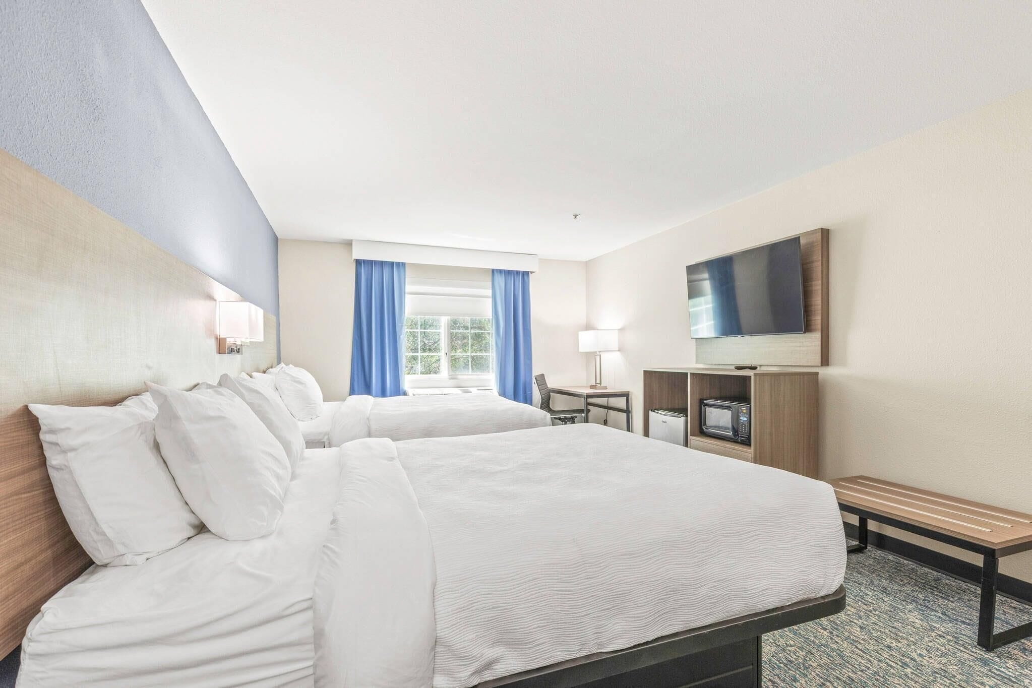 Habitación de hotel con dos camas, un escritorio, televisor y microondas.
