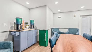 A conference room with a wooden table, blue chairs, a grey cabinet with a recycling bin, and two coffee machines.