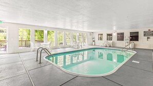 Una piscina interior con paredes de vidrio transparente, sillas blancas y una estación de salvavidas.