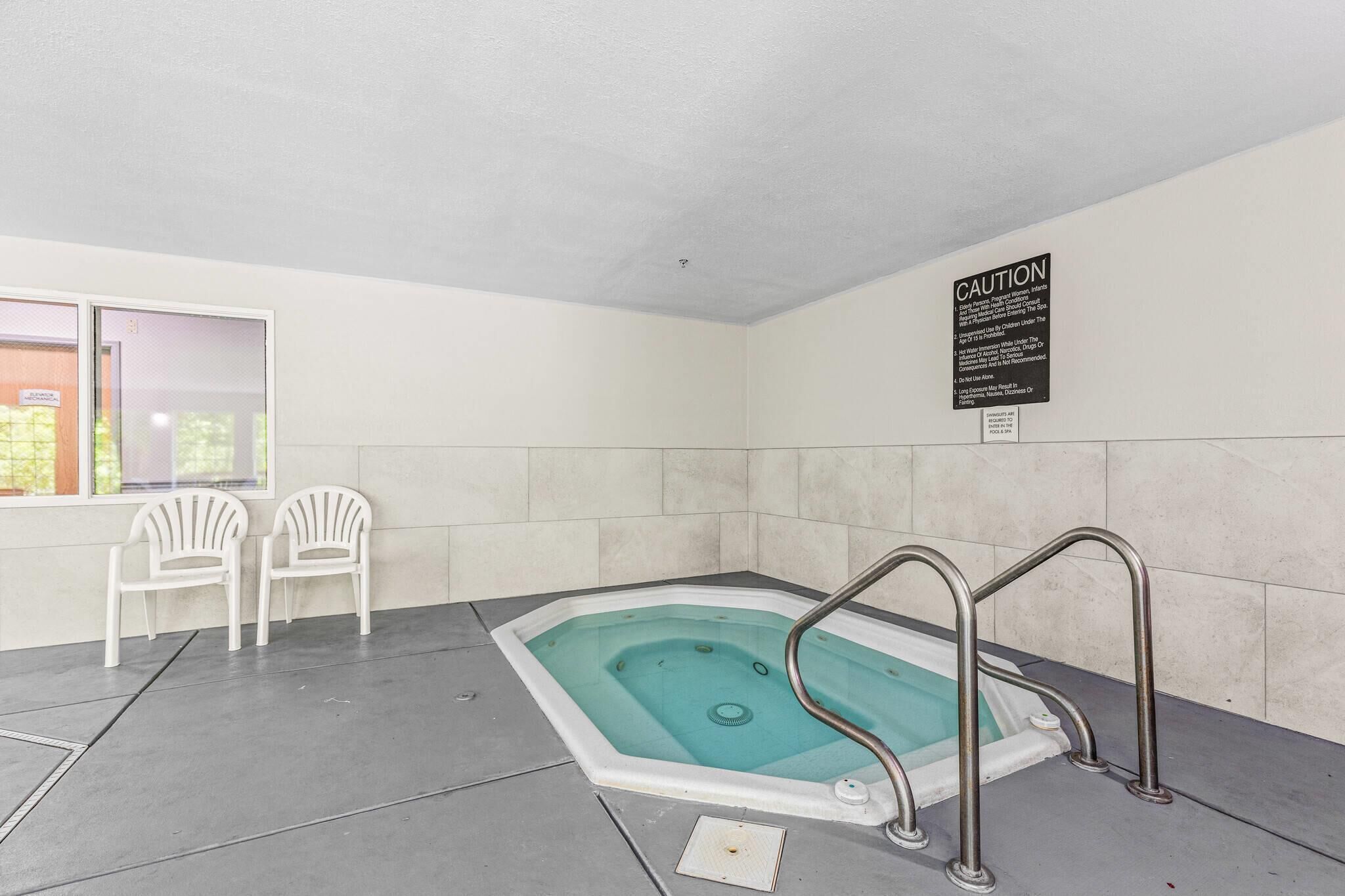 A small indoor pool with a caution sign, two white chairs, and a window.