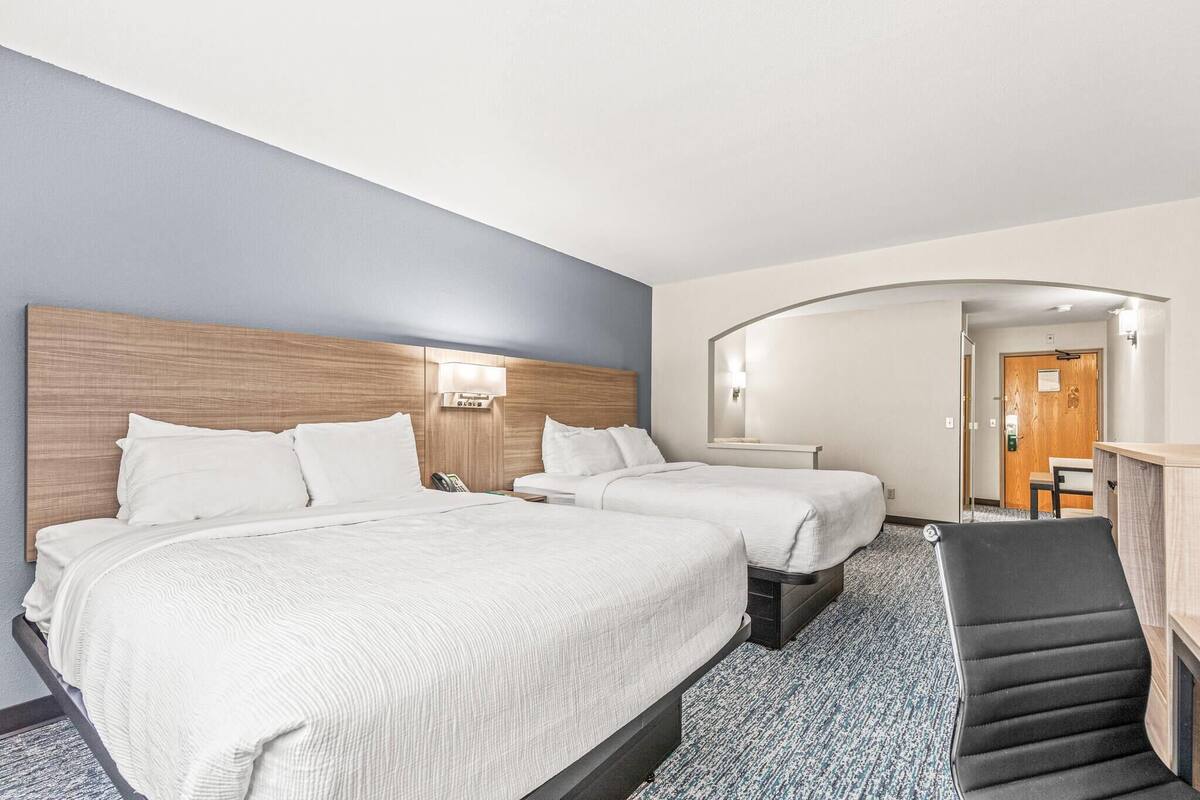 A hotel room with two beds, a desk, and a chair.