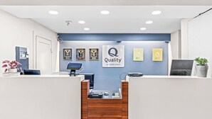 Un mostrador de recepción de hotel con pared azul, premios enmarcados, un letrero que dice 'Quality by Choice Hotels', una computadora y una máquina de café.