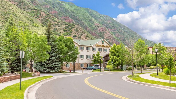 Un hotel con techo verde, rodeado de árboles y una montaña al fondo.