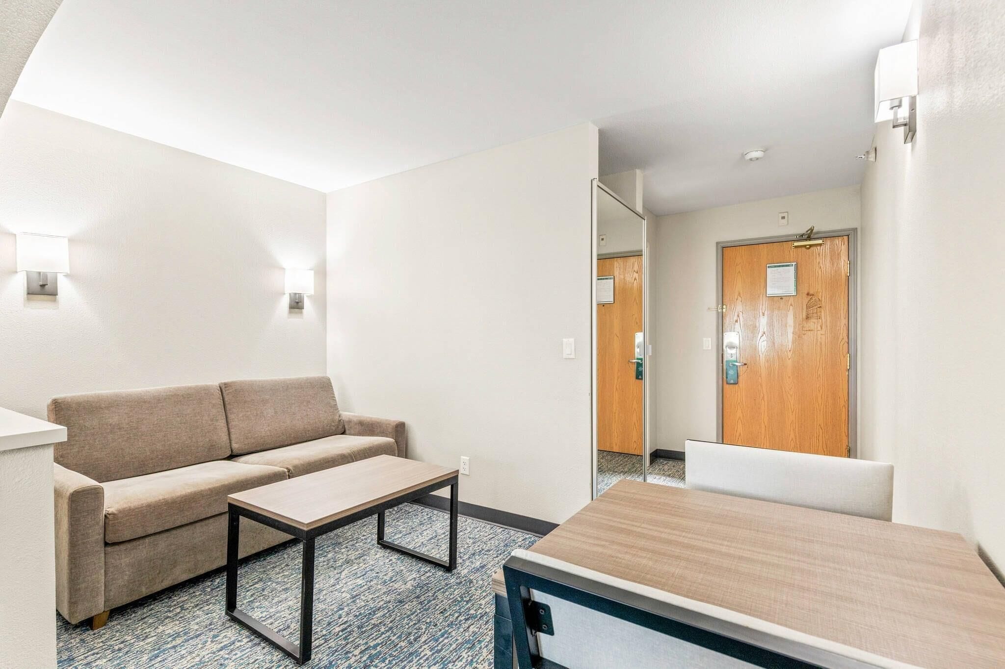 A hotel room with a sofa, a small table, a wooden desk, and a door with a mirror.