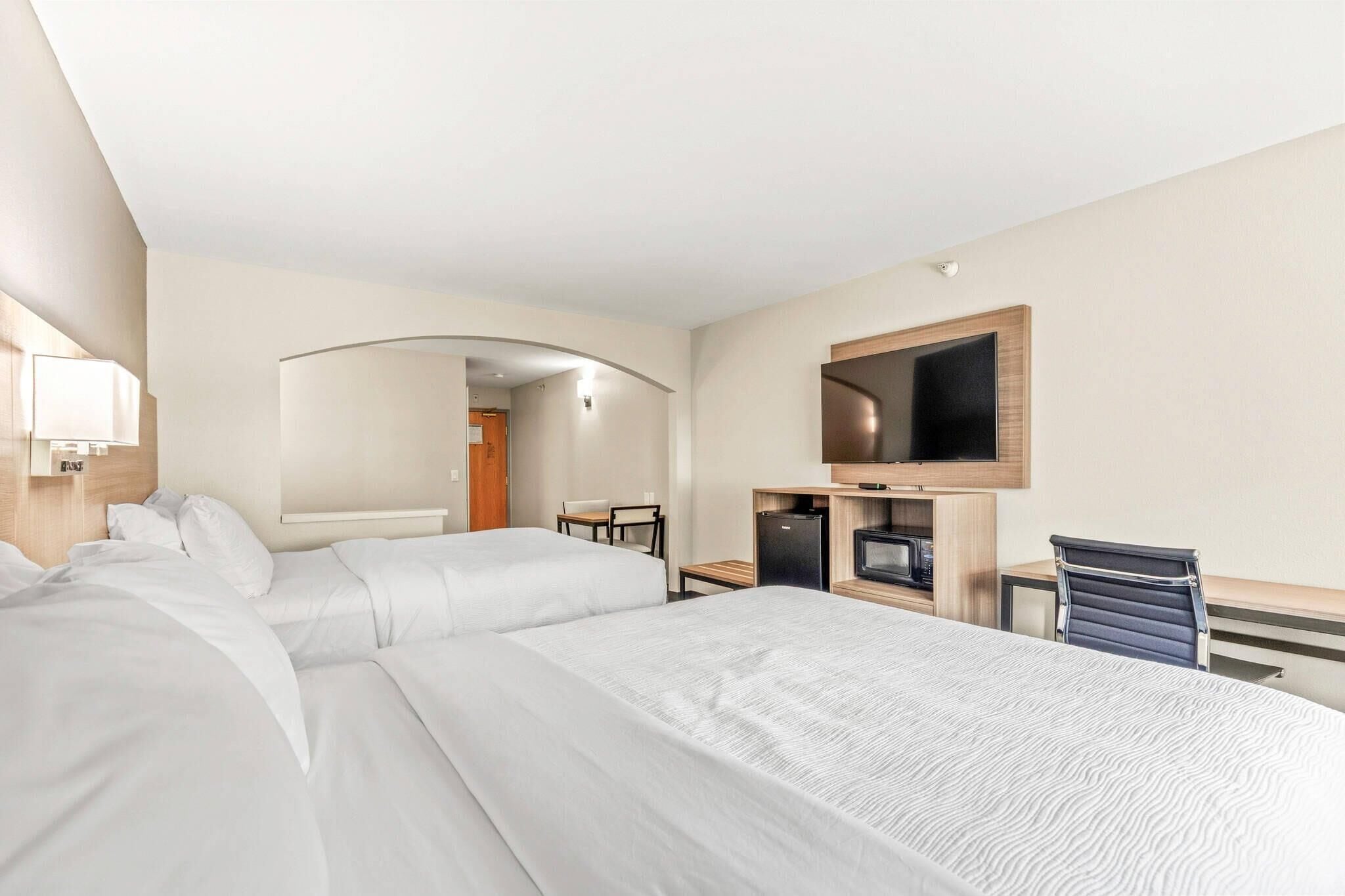 A hotel room with two beds, a desk, a TV, and a mirror.