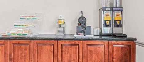 Et tekøkken med vaffeljern, kaffemaskine og en dispenser til glutenfri vafler.