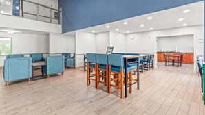 Amplia sala de estar con asientos tapizados en azul, una mesa de comedor de madera y una cocina al fondo.