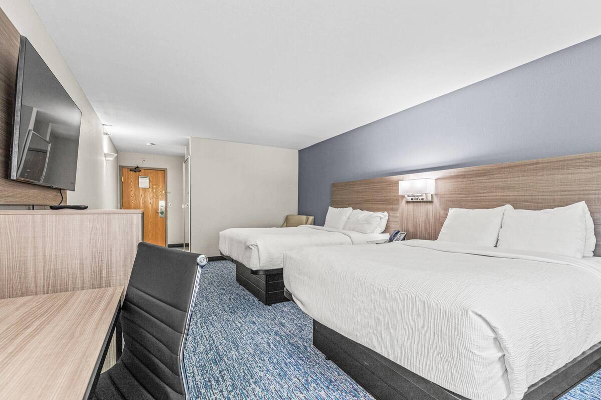 A hotel room with two beds, a desk, and a television.