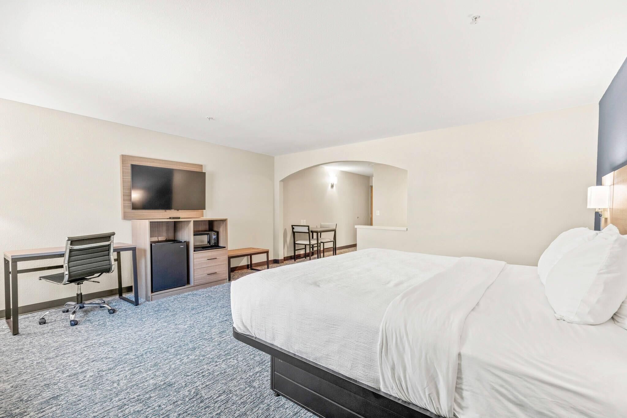 Habitación de hotel con cama, escritorio, silla, televisor y una kitchenette pequeña.