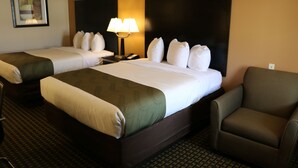 A hotel room with two beds, a nightstand with a lamp, a chair, and a patterned carpet. - Highland Inn (Gonzales)