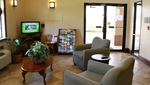 A lobby with a reception desk, a television, a bulletin board, and seating areas. - Highland Inn (Gonzales)