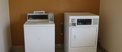 Two white laundry machines in a corner with a brown wall and tiled floor.