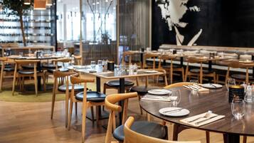 A restaurant interior with wooden tables and chairs, neatly set dining tables, and a large wall mural.