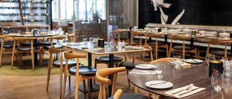 A restaurant interior with wooden tables and chairs, neatly set dining tables, and a large wall mural.