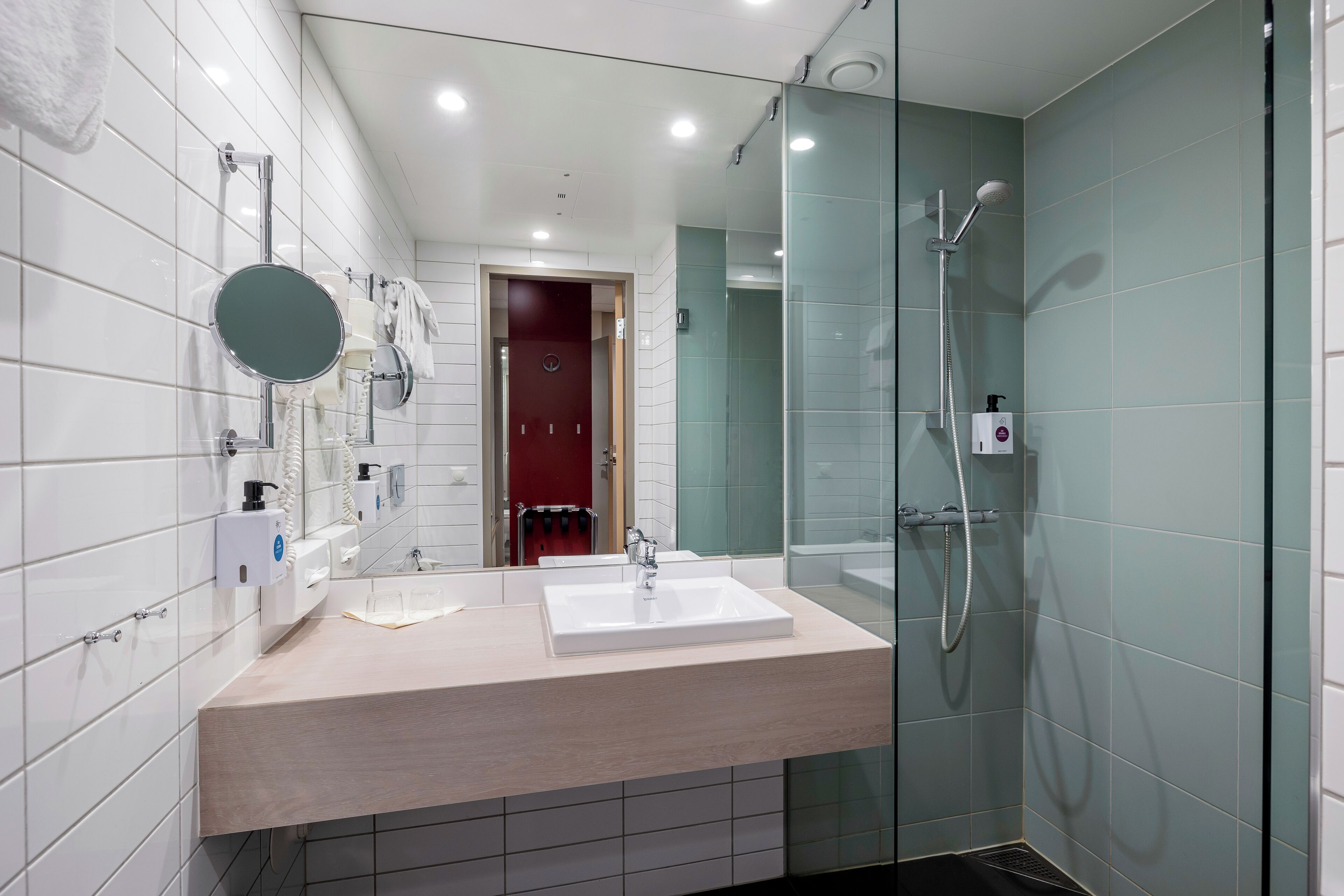 Un baño moderno con un lavamanos grande, un espejo, cabina de ducha con paredes de vidrio y paredes con azulejos blancos.