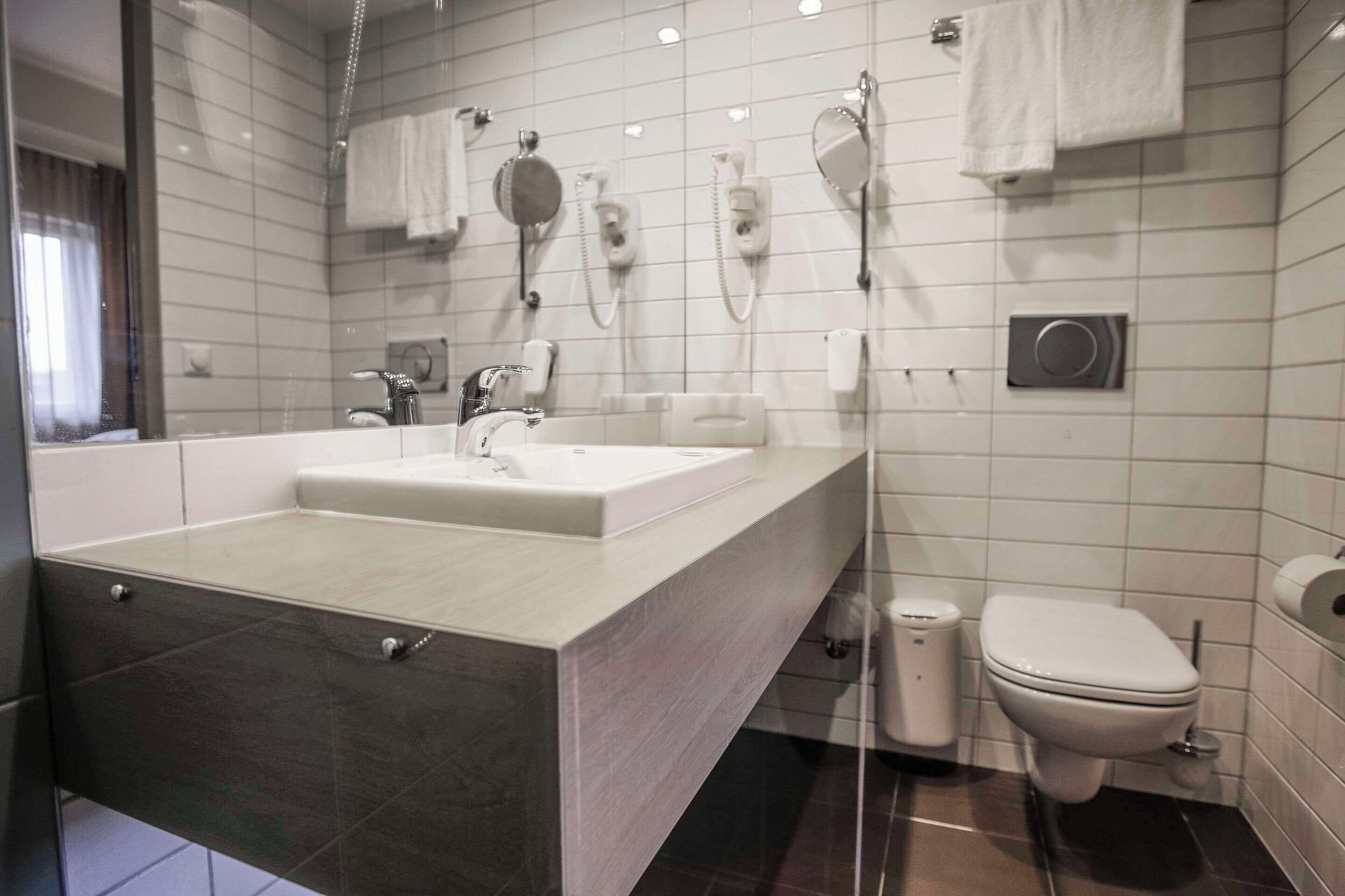 A modern bathroom with a large sink, two mirrors, a toilet, and a trash bin.