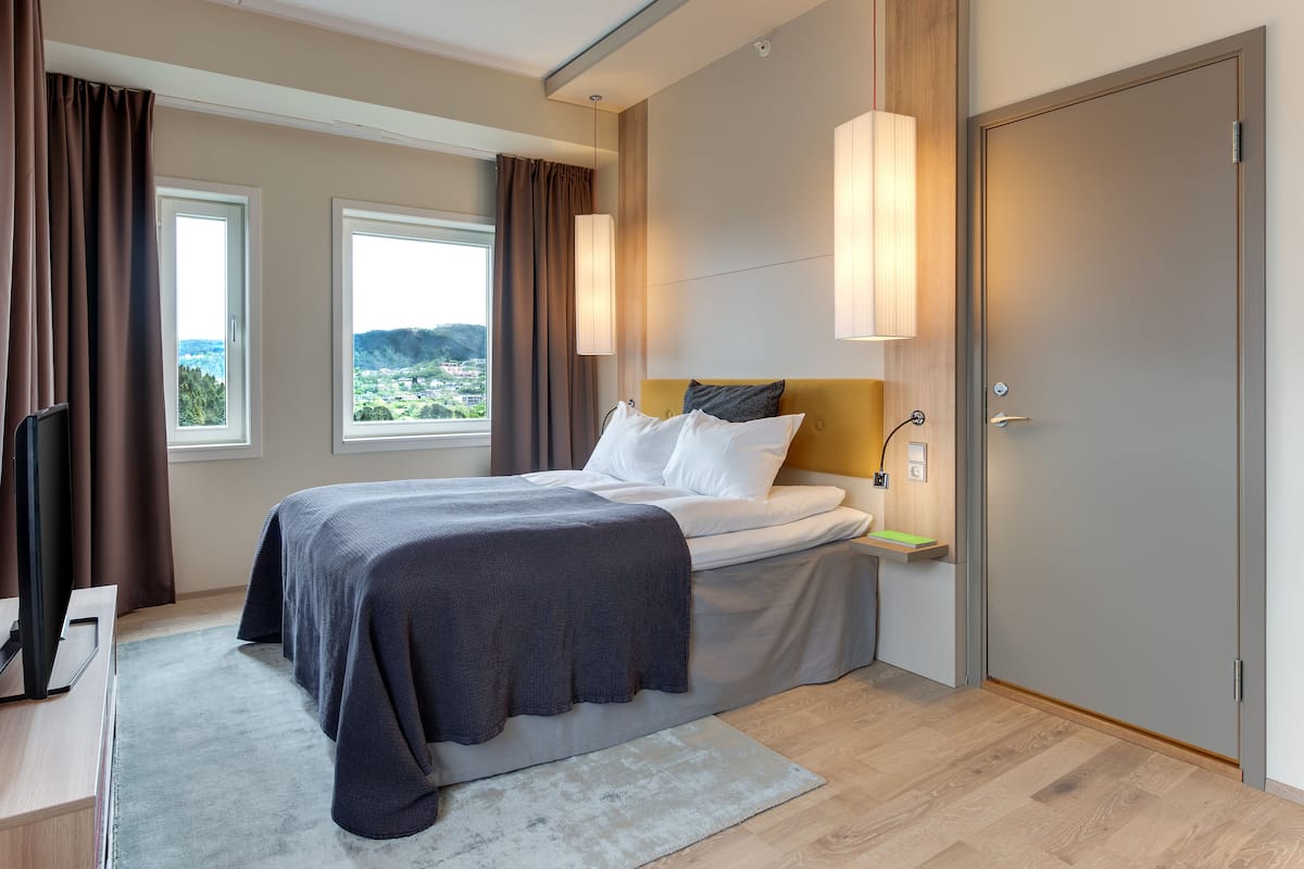 Ein modernes Hotelzimmer mit Bett, Schreibtisch, Fernseher und Blick auf die Stadt.