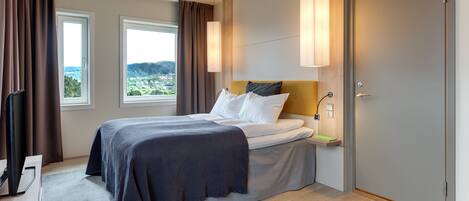 A modern hotel room with a bed, a desk, a TV, and a view of the city.
