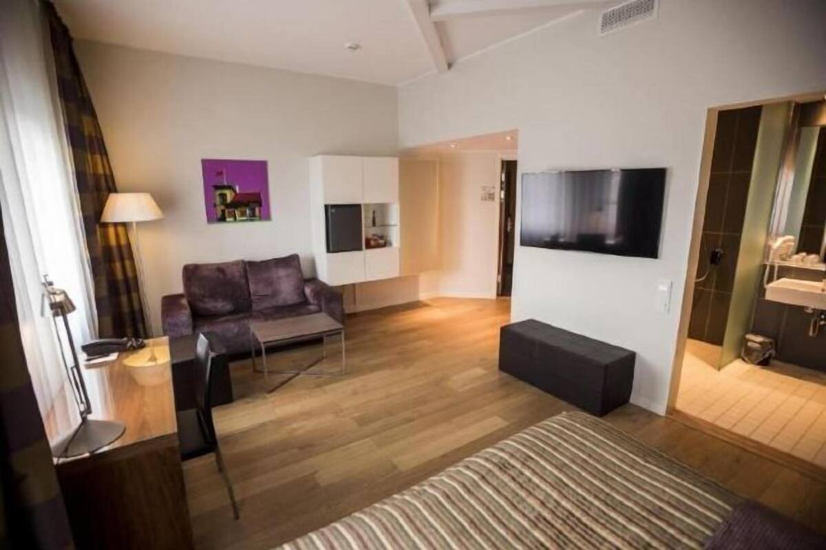 Ein modernes Wohnzimmer mit einer Couch, einem Couchtisch, einem an der Wand befestigten Fernseher und einer Küchenzeile im Hintergrund.