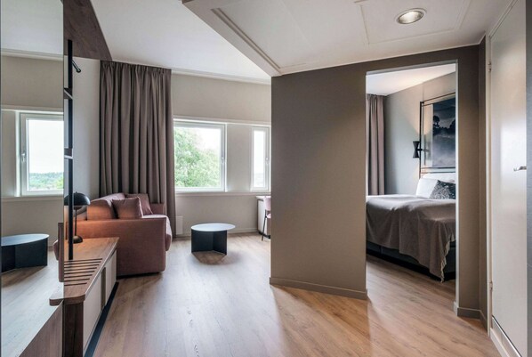 Una habitación de hotel moderna con sofá, una pequeña mesa redonda, cama y una ventana grande.