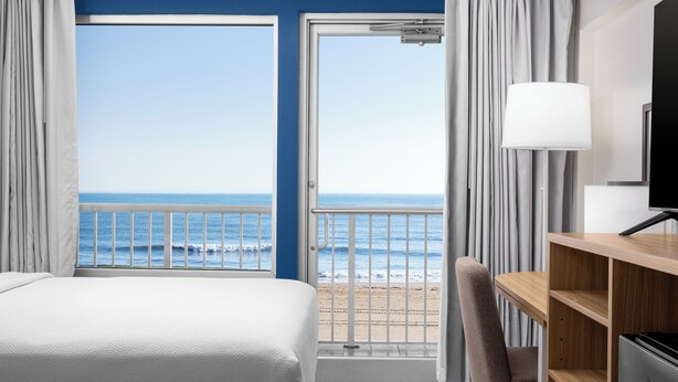 A hotel room with a bed, a desk, a chair, a TV, and a balcony with a view of the sea. - Spark by Hilton Virginia Beach Oceanfront (Virginia Beach)