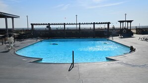 A rectangular pool with a surrounding deck, a wooden fence, and a view of the beach. - Spark by Hilton Virginia Beach Oceanfront (Virginia Beach)