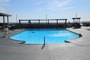 Uma piscina retangular com um deck ao redor, cerca de madeira e vista para a praia.