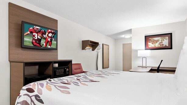 Habitación de hotel con una cama grande, un televisor de pantalla plana montado en la pared, un escritorio con lámpara y un cuadro enmarcado.