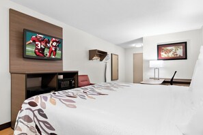 Une chambre d’hôtel avec un grand lit, un téléviseur à écran plat fixé au mur, un bureau avec une lampe et un tableau encadré au mur.