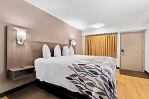 Ein Hotelzimmer mit einem großen Bett, einem Nachttisch, einer Wandleuchte und einer mit Vorhängen versehenen Tür.