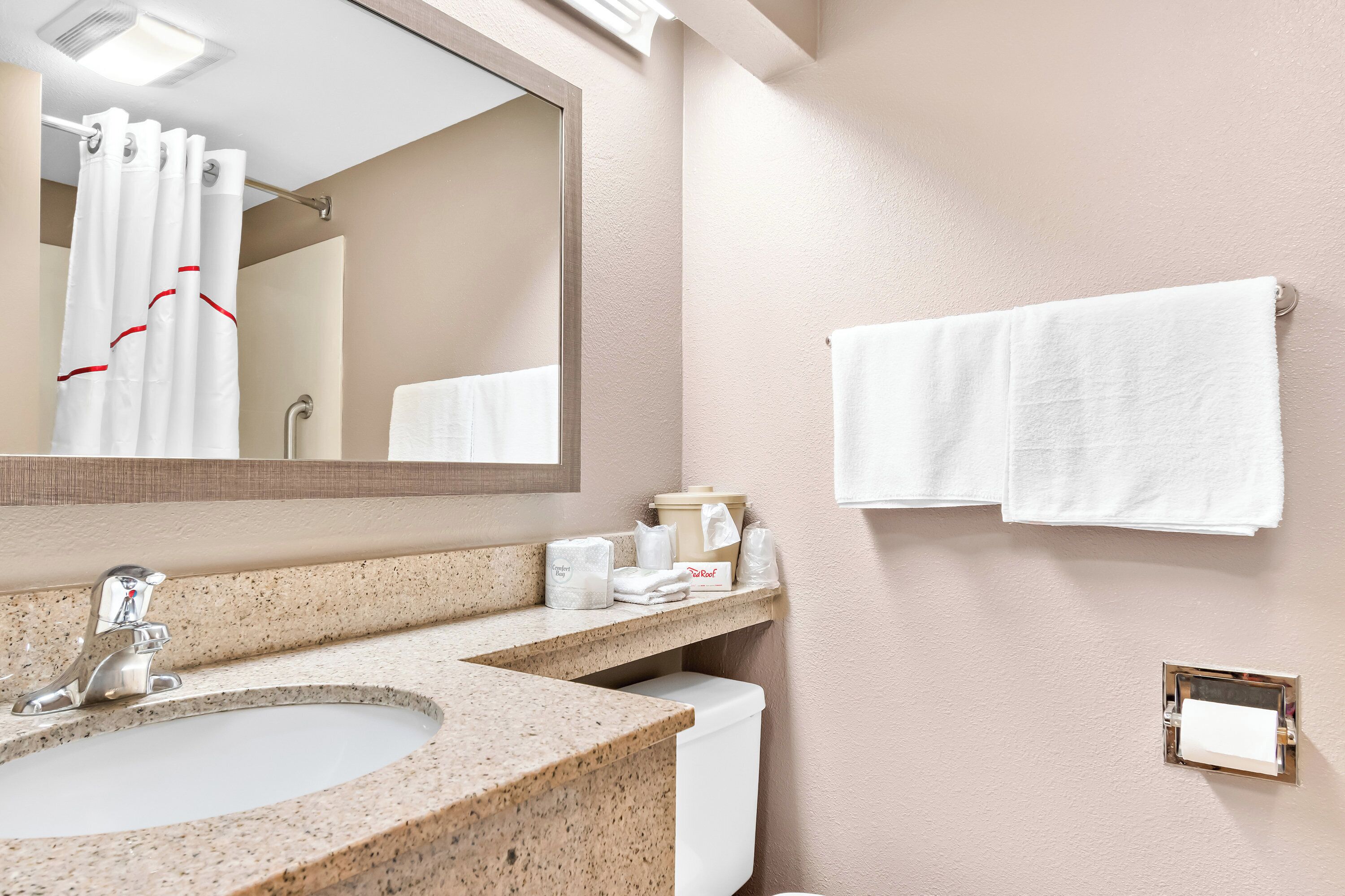 Une salle de bain avec un lavabo doté d’un plan de travail en granit, un miroir, un porte-serviettes avec deux serviettes blanches et des toilettes.
