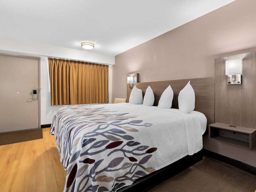 Een hotelkamer met een groot bed, een nachtkastje, een wandlamp en een deur met een gordijn.