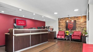Zona de recepción de Red Roof Inn con un mostrador de madera, un cartel que dice 'Wi-Fi gratuito en todas las habitaciones' y sillas rojas.