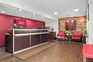 Een receptie van Red Roof Inn met een houten balie, een bord met 'Gratis Wi-Fi in alle kamers' en rode stoelen.
