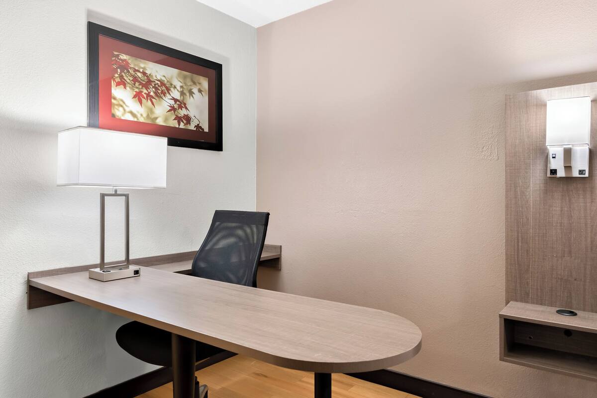 Une chambre d’hôtel moderne avec un bureau en bois, une chaise, un tableau encadré au mur et une étagère intégrée.