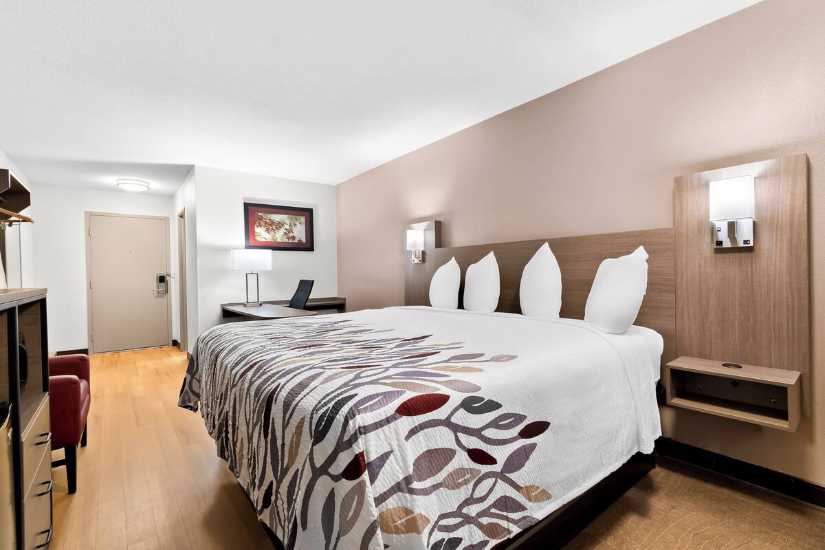 Une chambre d’hôtel moderne, dotée d’un grand lit, d’un bureau, d’une chaise et d’une étagère fixée au mur.