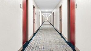 Un largo y estrecho pasillo de hotel con puertas rojas a ambos lados y una alfombra estampada.