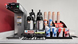 Una estación de café con una máquina de café Bunn, dispensador de agua caliente y diversas opciones de café y crema.