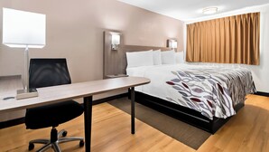 A hotel room with a bed, a desk, a chair, a lamp, and a wall-mounted light fixture. - Red Roof Inn Harrisburg North (Harrisburg)