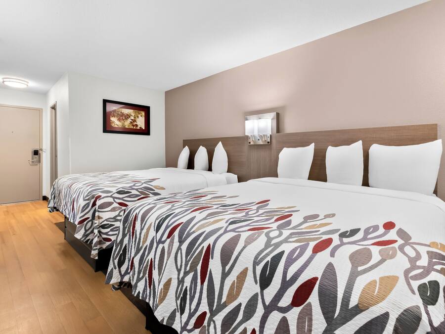 A hotel room with a large bed, a bedside table, a wall-mounted light, and a door.