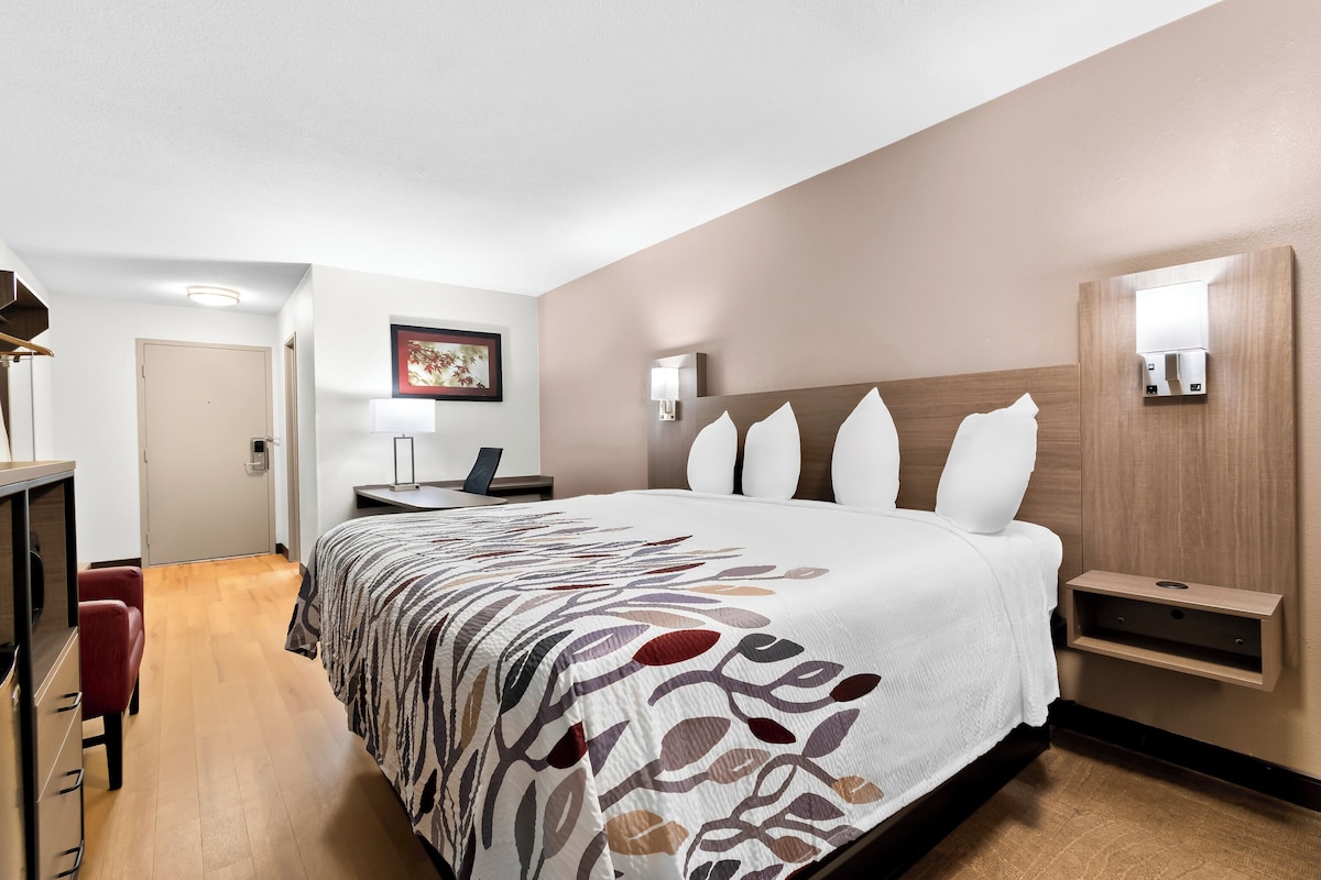 Ein modernes Hotelzimmer mit einem großen Bett, einem Schreibtisch, einem Sessel und einem Wandregal.
