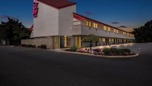 A modern hotel with a red roof and a neon sign. It has a large parking lot and a well-maintained garden with colorful flowers. - Red Roof Inn Harrisburg North (Harrisburg)