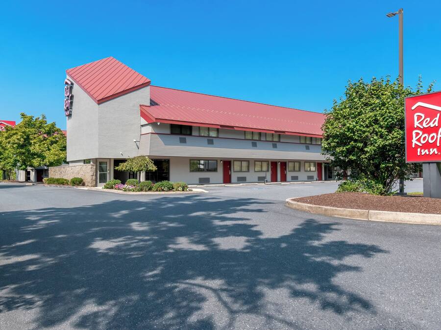 A Red Roof Inn with a red roof, a parking lot, and a clear blue sky.